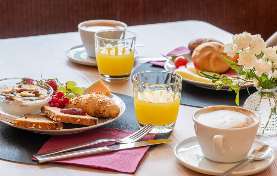 A breakfast with fresh rolls, cold cuts, muesli, fruit, coffee, and juice on a white table