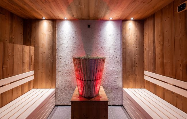 Moderner Wellnessbereich mit Holzwänden, Steinboden, Sitzgelegenheiten und einer Saunatür